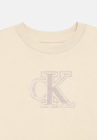 Κρεμ μπλούζα από βαμβάκι με απαλό, τυπωμένο λογότυπο "CK" σε ασημί χρώμα. Στρογγυλή λαιμόκοψη και κοντά μανίκια με λεία υφή.