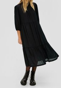 Svart midi-klänning med lagerdesign, lös passform och puffärmar. Buren med svarta snörstövlar för en kontrasterande textur.