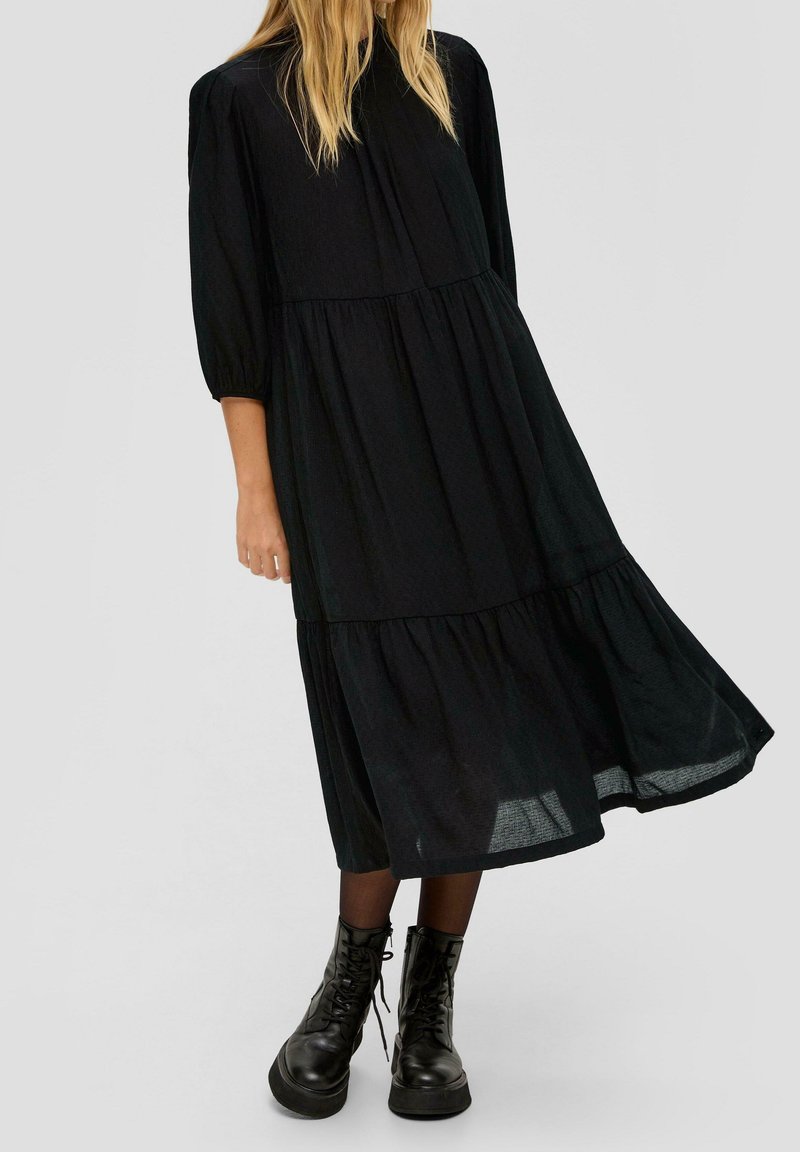 Svart midi-klänning med lagerdesign, lös passform och puffärmar. Buren med svarta snörstövlar för en kontrasterande textur.