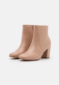 Stivali alla caviglia in ecopelle nudi con punta a punta, zip laterale e tacco chunky. Texture liscia, design minimalista e senza hardware visibile.