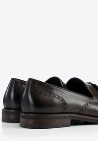Zapatos de cuero marrón oscuro con perforaciones decorativas a lo largo de los bordes. Punta redondeada, tacón bajo apilado y un acabado suave y pulido.