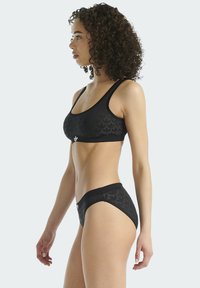 Czarny zestaw sportowy z biustonoszem i majtkami bikini, ozdobiony fakturowanym liściastym wzorem, elastycznymi paskami oraz logo marki na przednim pasku w talii.