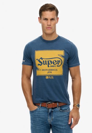 Mørkeblå bomuld T-shirt med en gul grafik med teksten "Super Dry Motorbikes JPN" og en tekstureret baggrund. Kortærmet, rund hals.