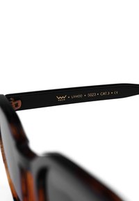 Hnědé želvovinové sluneční brýle s černými stranami. Zlatý gravírovaný text na stranách obsahuje značku, UV400 a certifikační detaily.