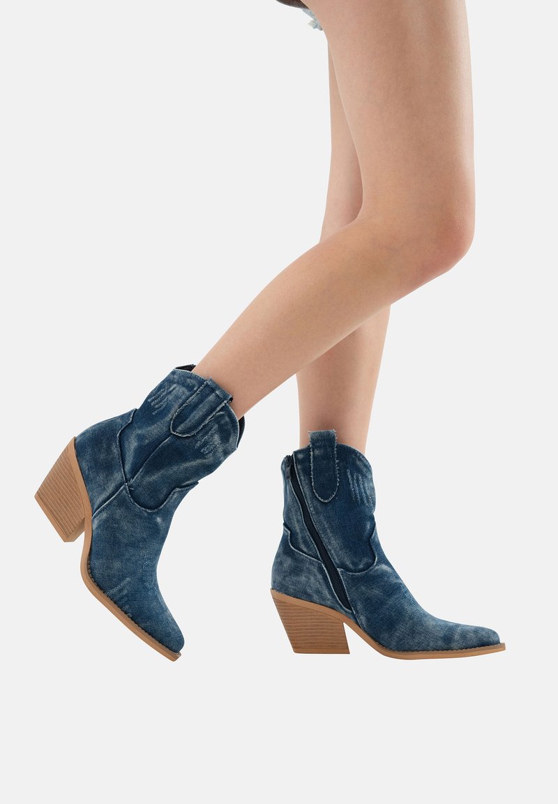 Botas vaqueras de denim con punta afilada, color azul desgastado, tacón de madera apilada y detalle de cremallera lateral para facilitar su uso.