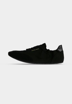 Baskets décontractées noires avec lacets, semelle lisse et petit logo doré "Michael Kors" sur le côté, présentées de profil sur fond blanc.