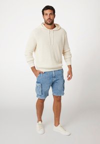Crème gebreide hoodie met trekkoord, gecombineerd met lichtblauwe cargoshorts met zijzakken, en witte sneakers.
