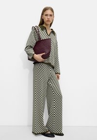 Ensemble de chemise et pantalon à carreaux verts et blancs avec un col, associé à un sac fourre-tout texturé violet foncé. Des ballerines noires complètent la tenue.