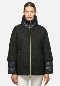 Giacca nera spessa e strutturata con colletto e polsini imbottiti blu lucido. Presenta una cerniera dorata e un design comodo.