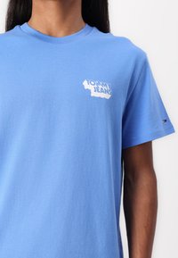 T-shirt en coton bleu avec un logo blanc "Tommy Jeans" sur la poitrine gauche et un petit accent rouge et blanc sur la manche.