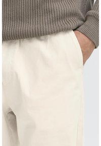 Pantalones beige de algodón con bolsillos laterales, con un corte recto y una textura suave, combinados con un suéter gris acanalado.