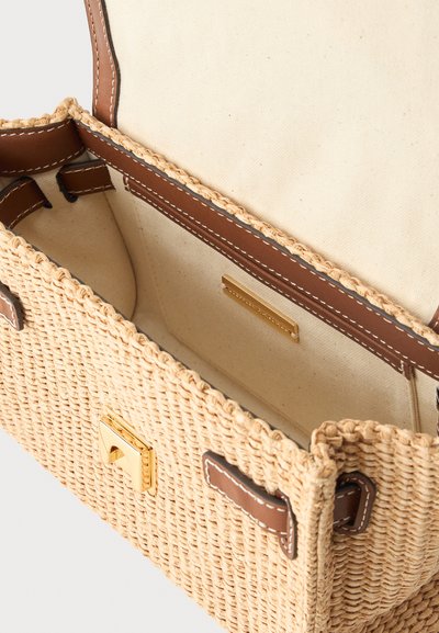 Πλεκτή τσάντα από άχυρο με καφέ δερμάτινη επένδυση, χρυσό κούμπωμα και μπεζ υφασμάτινη εσωτερική επένδυση που δείχνει έναν άδειο κύριο χώρο.