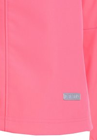 Sección de tela rosa brillante con costuras visibles y una pequeña etiqueta de marca rectangular reflectante cerca del borde inferior.