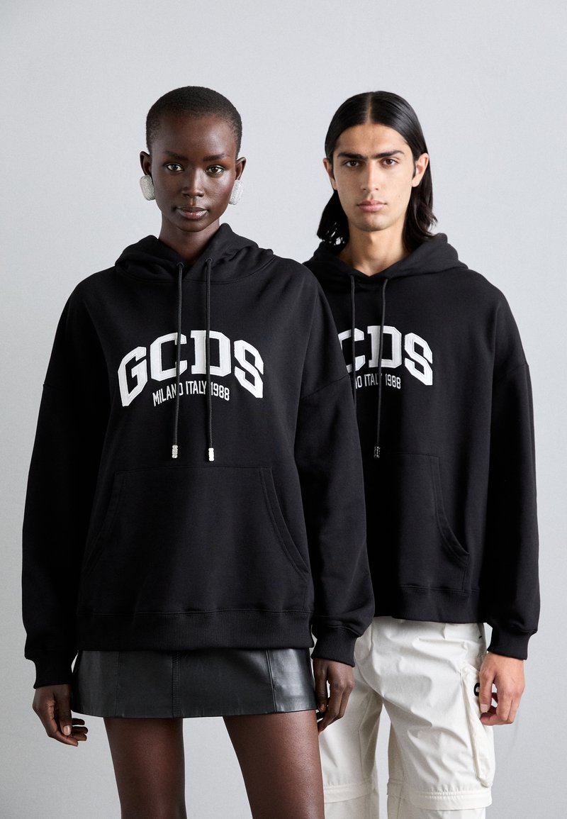 Felpe nere con logo "GCDS" e testo "1998" sul davanti. Presentano lacci, tasca a marsupio e polsini a coste. Il modello indossa una gonna di pelle.