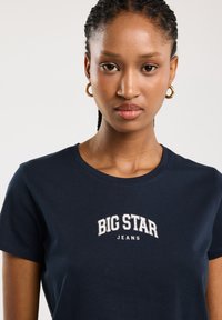 Náměsíčná modrá bavlněná tričko s krátkými rukávy a kulatým výstřihem. Na přední straně je bíle vyšitý text "BIG STAR JEANS".