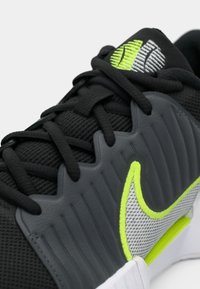 Μαύρο αθλητικό παπούτσι με γκρίζες πινελιές, διαθέτοντας υφή στη πάνω επιφάνεια, νεόν πράσινο λογότυπο και λευκή σόλα σε αντίθεση. Σχεδίαση με κορδόνια για ασφαλή εφαρμογή.