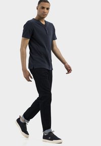 Chemise henley à manches courtes navy avec une patte à trois boutons, associée à un jean en denim foncé et des baskets navy avec des semelles plus claires.