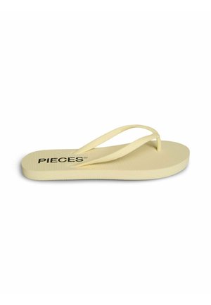 O singură papucă flip-flop de culoare galben deschis, cu talpă texturată și barete subțiri, numele mărcii „PIECES” imprimat aproape de călcâi.