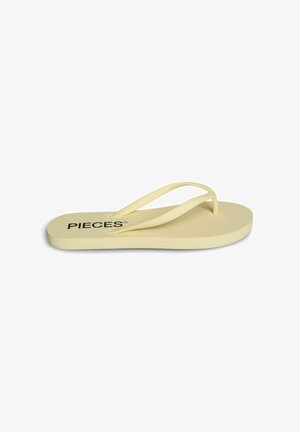 O singură papucă flip-flop de culoare galben deschis, cu talpă texturată și barete subțiri, numele mărcii „PIECES” imprimat aproape de călcâi.
