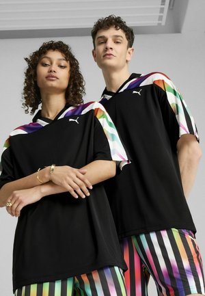 Černé trička Puma s barevnými proužkovanými rukávy. Design má V-výstřih a volný střih. Modelky nosí proužkované kalhoty v živých barvách.