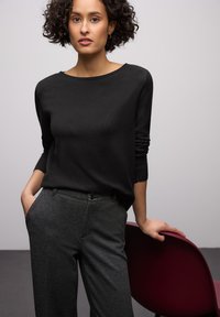 Schwarzer Pullover mit U-Boot-Ausschnitt und gerippten Bündchen, kombiniert mit dunkelgrauen Hosen mit Frontknopf und Taschen. Glatte Texturen.