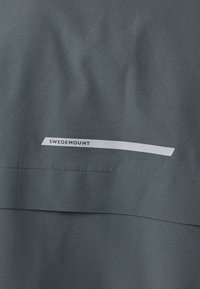 Ciemnoszara tkanina z poziomym szwem i małą białą prostokątną metką z napisem „SWEDEMOUNT” w pobliżu środka.