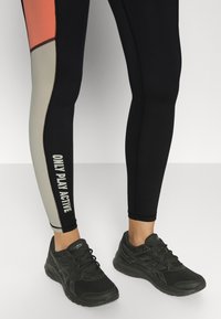 Leggings sportivi neri con dettagli in corallo e beige; presenta il testo "ONLY PLAY ACTIVE" in bianco. Abbinati a scarpe da ginnastica nere.
