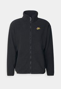 Svart fleece zip-up jacka med hög krage, med en gul Nike-logga på vänster bröst. Mjuk textur, långa ärmar, vanlig passform.