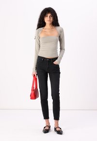 Ljusgrå långärmad topp, figurnära, i kombination med högmidjade svarta jeans. Modell som håller en röd rektangulär handväska, bär svarta platåskor med nitar.