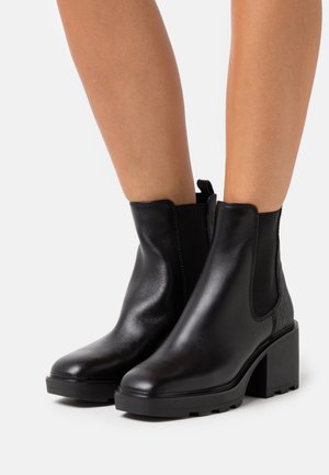 Mustat nahkaiset nilkkurit, joissa on paksut korot, joustavat sivupaneelit ja teksturoidut takakoristeet. Sileä pinta, pyöreä kärki ja tukeva pohja.