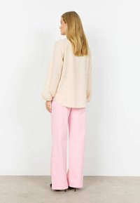 Laza szabású bézs blúz virágos hímzéssel, magasderekú, rózsaszín, bő szárú nadrággal párosítva. Sima textúra és kényelmes sziluett.