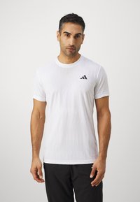 Valge lühikeste varrukatega spordipaita tekstuuriga mustriga ja musta Adidas logo vasakul rinnal. Ümar kaelus, kerge kangas.
