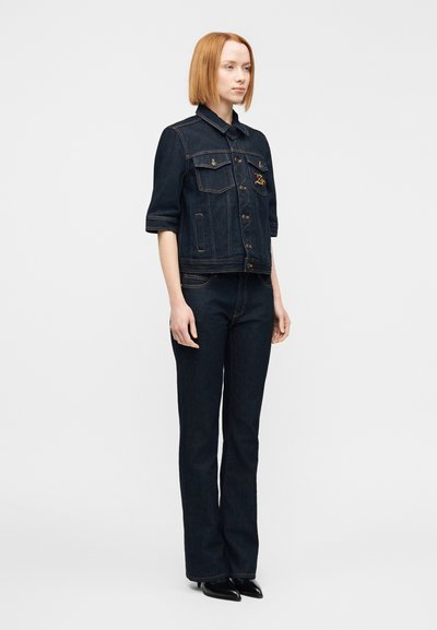 Μπλε τζιν μπο υφάν με γιακά, κοντά μανίκια και μπροστινές τσέπες. Συνδυάζεται με σκούρα τζιν παντελόνια καμπάνα και μαύρα μυτερά παπούτσια.