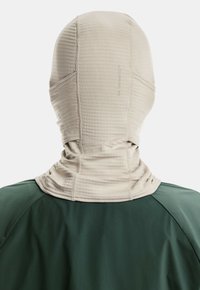 Person wearing a beige full-face balaclava with stitched panels and a green jacket, shown from behind against a white background.