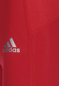 Rote Sportshorts aus dehnbarem Material mit glatter Textur. Mit einem silbernen Adidas-Logo und dezenten Perforationsakzenten.