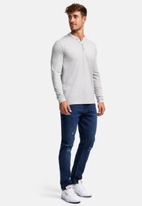 Svijetlo siva dugosleeve henley majica s tri gumba, u paru s poderanim tamnoplavim trapericama i bijelim tenisicama. Glatka tekstura tkanine.