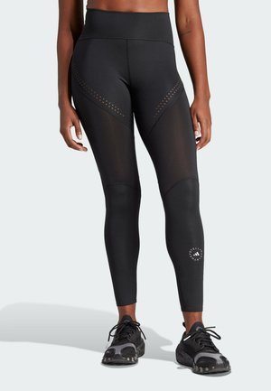Athlete wearing black high-waisted leggings with mesh panels and perforated details, paired with black and gray running shoes.