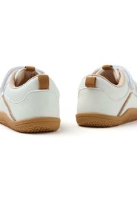 Baskets en cuir blanc avec une semelle en caoutchouc beige, présentant un onglet de talon texturé et des détails. Le design inclut un profil bas et une forme courbée.