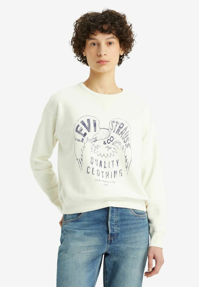 Felpa bianca con collo rotondo, caratterizzata da una stampa grafica di "Levi Strauss & Co." e un design di aquila in blu scuro. Abbinata a jeans blu.