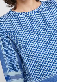 Sininen kuvioitu neulepaita, jossa on geometrinen muotoilu ja teksturoidut hihat. Valmistettu pehmeästä kankaasta, jossa on pyöreä pääntie ja rento sovitus.