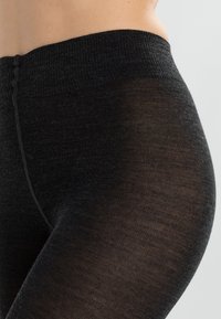 Czarne legginsy wykonane z teksturowanej tkaniny z wysokim stanem. Materiał wydaje się elastyczny i dopasowany, prezentując gładką powierzchnię.