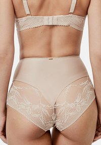 Soutien-gorge beige et culotte taille haute en dentelle et tulle. Finition en dentelle au dos avec des motifs floraux. Bretelles ajustables, fermeture à crochets et œillets.