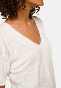 White cotton blend top featuring a deep V-neck and short sleeves, with a soft, textured finish and relaxed fit.