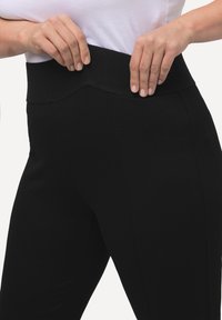 Leggings neri con una vita larga e testurizzata. Il tessuto sembra liscio ed elastico, con cuciture visibili e un design aderente.