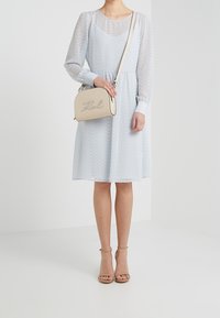 Ljusblå prickig klänning med lång ärm och midjeband, ihop med en liten beige handväska med ett skriptlogotyp och bruna sandaletter med remmar.
