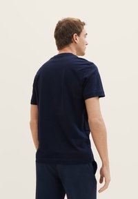 Navy-blaues Baumwoll-T-Shirt mit kurzen Ärmeln, Rundhalsausschnitt und lockerer Passform. Sichtbare Nähte und seitliche Schlitze am Saum.