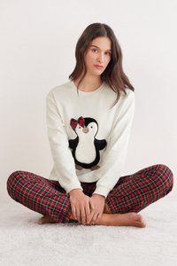 Sudadera blanca con un diseño de pingüino que presenta un lazo de cuadros rojos. Pantalones de pijama de cuadros rojos y negros. Textura suave, diseño casual.