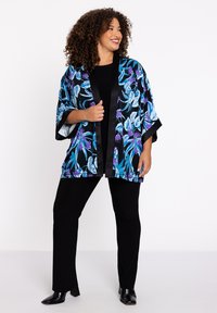 Zwart kimono met bloemenpatroon, gekenmerkt door blauwe en paarse bloemen, satijnen afwerking en wijde mouwen, gecombineerd met zwarte aansluitende broek en laarzen.