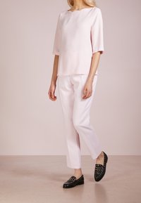 Ljusrosa kortärmad blus med en vågig halsringning, kombinerad med matchande ljusrosa byxor. Svarta loafers prydda med nitar.