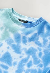 Svetlo modrý sveter s tie-dye vzorom. Má rebrový okrúhly výstrih a mäkkú textúrovanú tkaninu. Štítok viditeľný vo vnútri goliera.